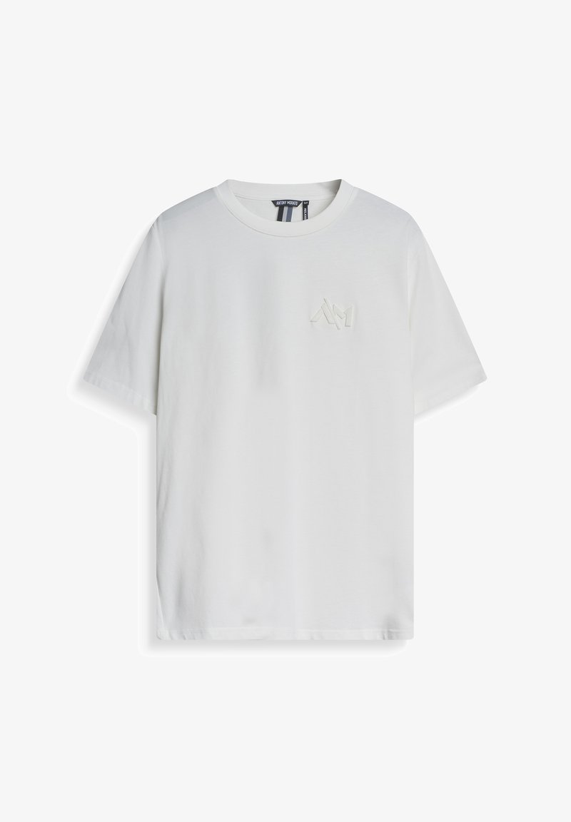 Camiseta de algodón blanco con mangas cortas, cuello redondo y un pequeño logo tono sobre tono en el lado izquierdo del pecho. Textura suave, corte casual.