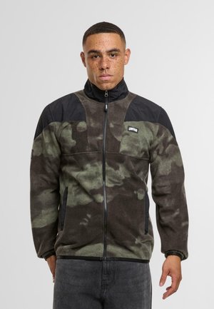 Veste en polaire dans un motif camouflage noir et vert foncé avec un col haut, fermeture éclair à l'avant et poches latérales, avec des emmanchures noires et un logo.