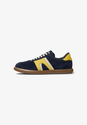 Navy suede sneakers with yellow and white accent stripes, flat brown rubber sole, and cream laces. Low-top design with cushioned collar.
