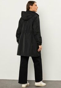 Giacca nera impermeabile con cappuccio, vita elastica e maniche lunghe, caratterizzata da una texture liscia e una vestibilità comoda.