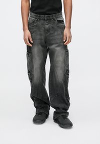 Crne traper hlače cargo kroja s opuštenim pristajanjem, s više bočnih džepova i teksturiranim izblijedjelim detaljima za istrošen izgled.