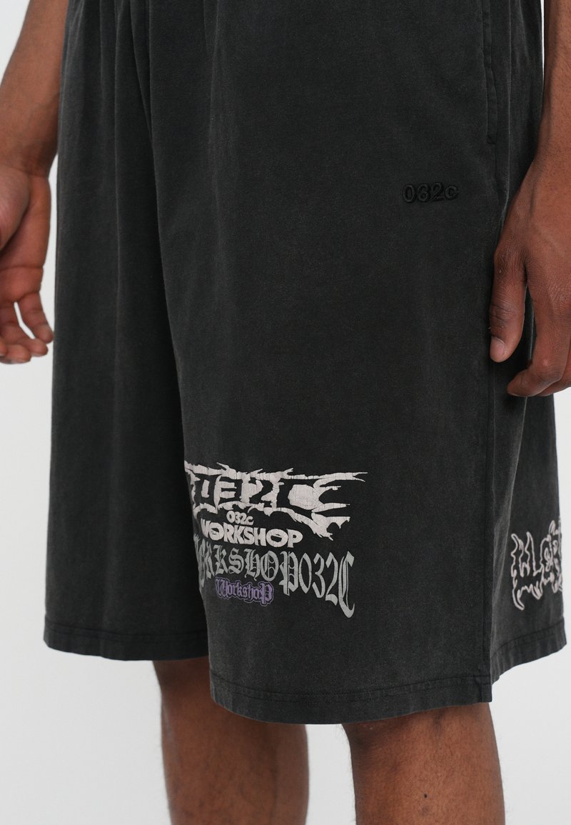 Pantalones cortos negros de tejido suave presentan estampados gráficos en blanco y púrpura con texto. El diseño incluye costuras sutiles y un dobladillo recto.