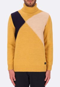 Maglione giallo a collo alto con blocchi di colore diagonali in blu navy, beige morbido e giallo testurizzato. Orlo e polsini a coste, tessuto lavorato a maglia.