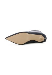 Scarpa nera in pelle con tacco alto, punta affilata, superficie liscia e suola piatta color beige chiaro con leggere scanalature e marchio.