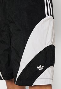 Svart-och-vitt Adidas-shorts med tre ränder på sidan och Adidas treklöverlogotyp broderad nära kanten.