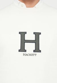 Felpa bianca con una grande "H" ricamata in grigio scuro e la parola "Hackett" sottostante. Realizzata in un tessuto morbido con una texture liscia.