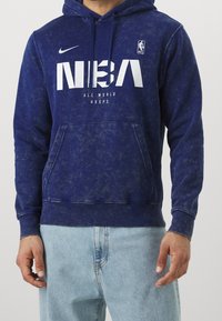 Sweat à capuche bleu marine avec une finition texturée, doté d'une poche kangourou à l'avant, d'une capuche avec cordon de serrage, et d'un grand logo NBA blanc accompagné de texte.