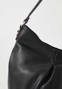 Sac en cuir noir avec une surface texturée, doté d'une seule bandoulière et d'un accent en métal doré près du haut.