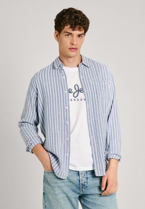 Hellblau-weißer gestreifter Hemd mit Knopfverschluss, getragen über einem weißen T-Shirt mit Druckschrift, kombiniert mit hellblauen Jeans.