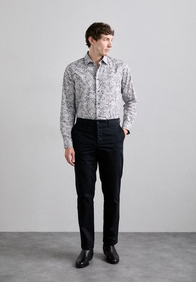 Fehér, lila és zöld virágmintás ing, fekete nadrággal és bőr csizmával párosítva. Slim fit szabású, hosszú ujjú.