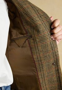 Pruun ruuduline bleiser, millel on tekstureeritud välimus ja silepruun vooder, koos tasku ja kontrastsete tumepunaste äärepindadega.