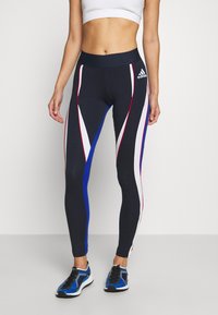 Laikennys urheiluleggingsit, joissa on punaisia, valkoisia ja sinisiä kulmikkaita viivoja; korkea vyötärö; sileä ja joustava kangas; yhdistetty mustiin ja sinisiin lenkkikenkiin.