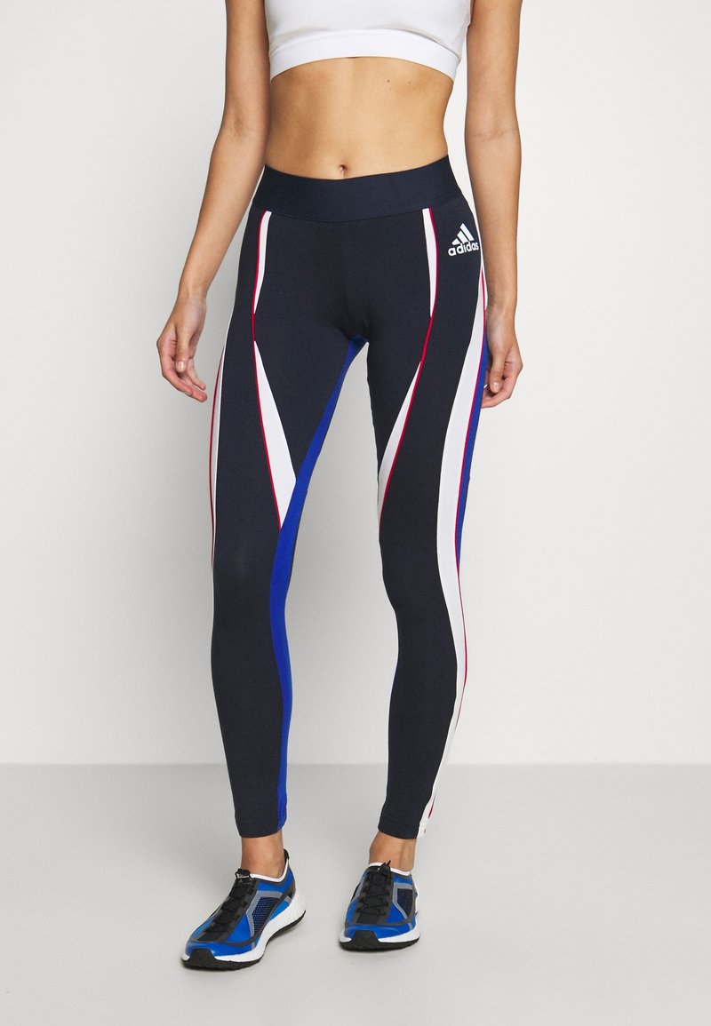 Laikennys urheiluleggingsit, joissa on punaisia, valkoisia ja sinisiä kulmikkaita viivoja; korkea vyötärö; sileä ja joustava kangas; yhdistetty mustiin ja sinisiin lenkkikenkiin.