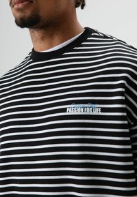 T-shirt à rayures noires et blanches avec un col rond et une broderie bleue "Passion for Life". Matière en coton doux.