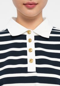 Námornícky a biely pruhovaný polo shirt s bielym golierom a štyrmi zlatými gombíkmi na prednej strane, s jemnou, textúrovanou tkaninou.