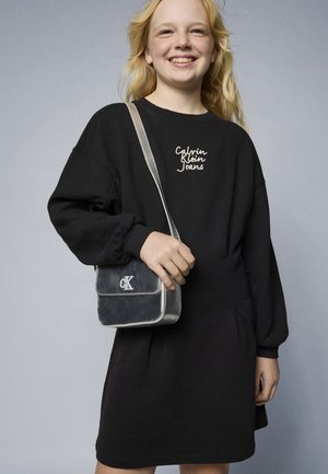 Mustmustel dress, milledega kogutud varrukatega, millel on valge "Calvin Klein Jeans" tikand. Koos hõbedastes aktsentides musta käekotiga.