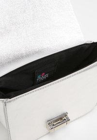 Stříbrné kovové psaníčko s hladkým povrchem, černou vnitřní podšívkou a obdélníkovým tvarem. Má zapínání na sponu s lesklým povrchem.