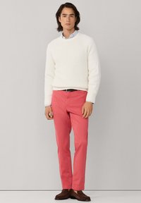 Witte ribgebreide trui, roze broek, zwarte riem en bruine schoenen. De trui heeft een ronde hals; de broek heeft rechte pijpen met een gladde textuur.