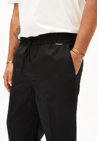 Zwarte relaxte broek gemaakt van zachte stof, met een elastische tailleband, verstelbaar koord en zijzakken. Minimalistisch ontwerp.