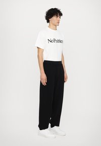 White cotton t-shirt with "No Problem" print, paired with black loose-fitting pants and white sneakers; minimal design, smooth texture.
