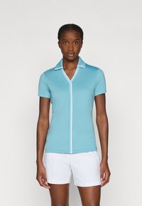 Světlomodré polo tričko s krátkým rukávem a V-výstřihem, bílé lemování a slim fit. V kombinaci s bílými šortkami, což zdůrazňuje sportovní vzhled.