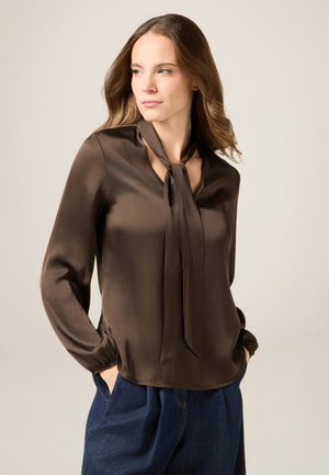 Bruine zijden blouse met een sleuf en een aangehechte strikdetail. Lange mouwen met geplooide manchetten. Gecombineerd met lichtblauwe denim broek.