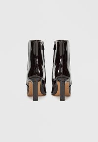 Botas de tornozelo em verniz preto com um salto quadrado, apresentam ziper com detalhe de franjas e textura lisa.