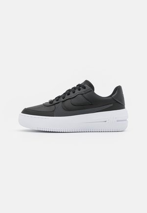 Black leather sneakers with textured details, flat laces, and a thick white sole. Features a visible logo and layered design.