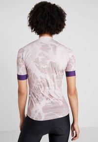 Kortärmad cykeltröja i ljusrosa med ett strukturerat abstrakt mönster, lila detaljer på ärmarna och en dragkedjeficka på baksidan.