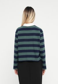 Ingekorte blouse met lange mouwen in marineblauw en groene horizontale strepen, voorzien van een witte kraag. Zacht katoenen materiaal met een comfortabele pasvorm.