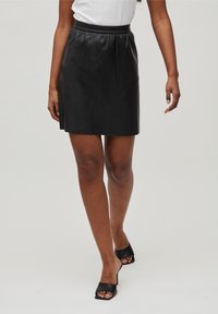 Zwarte leren minirok met een elastische tailleband, een gladde textuur en een eenvoudige A-lijn vorm. Draagt bij zwarte open hiel schoenen.