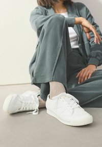 Hvide sports sneakers med teksturerede læderpaneler og gummisåler. Båret med lyse ribbede sokker og parret med en grå træningsdragt.