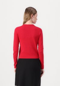 Maglione rosso a maniche lunghe con scollatura rotonda, realizzato in tessuto morbido. Presenta una silhouette aderente e polsini a costine, mostrato dalla parte posteriore.