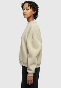 Beige genser med avslappet passform, rund hals og oversized ermer. Laget av mykt stoff, har ribbede mansjetter og kant.