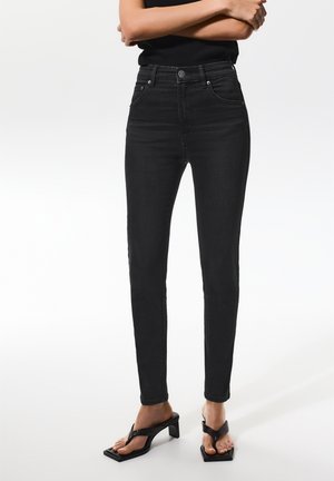 Jeans en denim noir taille haute avec une coupe slim, dotés d'une fermeture à bouton, de poches avant et d'un léger dégradé pour la texture.