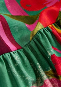 Gros plan d’un tissu froncé présentant des motifs floraux abstraits dans des tons vifs de vert, rouge, rose et jaune avec une texture visible.