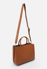 Sac fourre-tout en cuir brun avec deux poignées courtes et une bandoulière amovible, présentant une surface texturée et un design minimaliste.