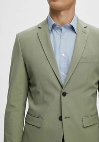 Light green suit jacket with a tailored fit, featuring a notched lapel, two front pockets, and a single button closure over a light blue shirt.