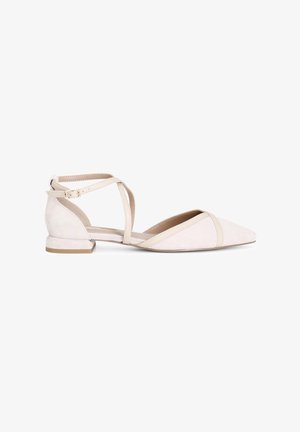Zapato plano de punta en suave ante beige claro con correas de tobillo entrecruzadas y un tacón bajo. Presenta un diseño minimalista con ribetes en contraste.