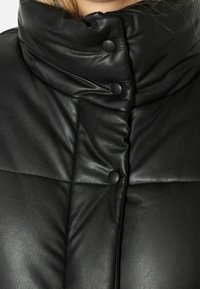 Černá kožená péřová bunda s vysokým límcem, textured povrchem a knoflíky podél přední části. Stehovaný design přidává vizuální zajímavost.