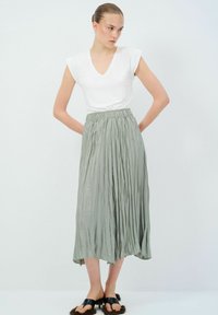 Gonna midi plissettata di colore verde chiaro, con vita elastica, abbinata a una maglietta bianca con scollo a V e sandali neri con apertura.