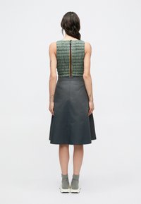 Mouwloze jurk met een groen gewatteerd textuur lijfje en een grijze uitlopende rok met een ritssluiting aan de achterkant.