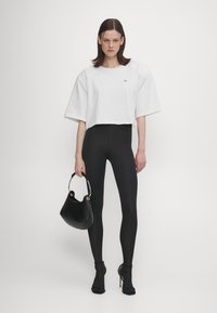 White cropped t-shirt with short sleeves, black leggings, and a black handbag with a silver handle. Model wearing black heeled booties.