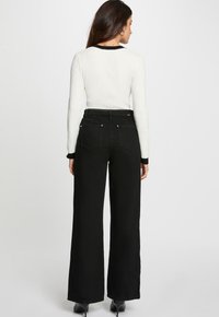 Jeans anchos negros de tiro alto, con una tela suave, diseño de cinco bolsillos y cinturilla de contraste. Combinados con una blusa blanca ajustada.
