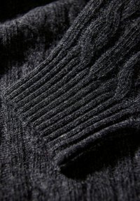 Czarny sweter z dzianiny o plecionce posiada ryflowaną teksturę i różnorodne wzory splotów, o miękkim, puszystym wyglądzie. Zbliżenie na szczegóły materiału.