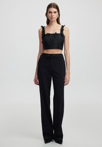 Černý crop top s květinovou texturou a detaily na ramínkách, spárovaný s černými kalhotami s vysokým pasem a rovnými nohavicemi s knoflíkovým zapínáním.