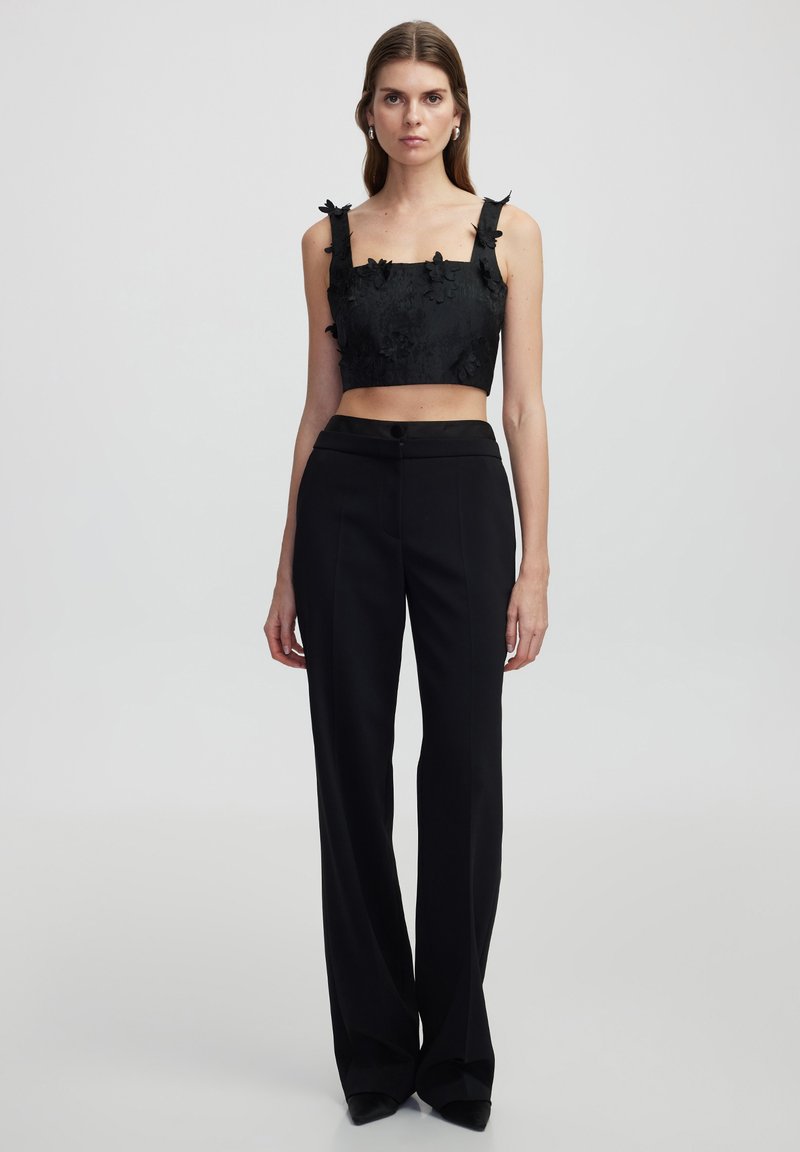 Černý crop top s květinovou texturou a detaily na ramínkách, spárovaný s černými kalhotami s vysokým pasem a rovnými nohavicemi s knoflíkovým zapínáním.