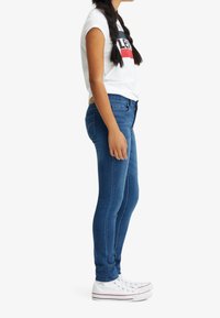 Jeans ajustados azules de denim, con un diseño estándar de cinco bolsillos. Combinados con una camiseta gráfica blanca y zapatillas blancas.