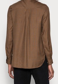 Camicia a maniche lunghe a quadri marroni e neri, con una vestibilità rilassata, orlo arrotondato e polsini con bottoni, realizzata in un tessuto leggero.