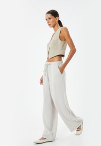 Gilet cropped beige avec un décolleté en V et une fermeture à bouton, associé à un pantalon large gris clair avec une taille élastique et des poches.